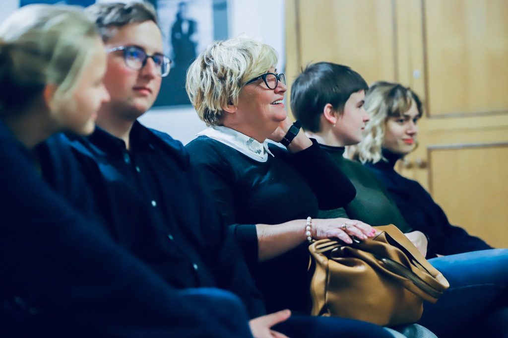 Uczestnicy spotkania, w tym kobieta w okularach i młodzież, uśmiechają się i rozmawiają w trakcie wydarzenia.